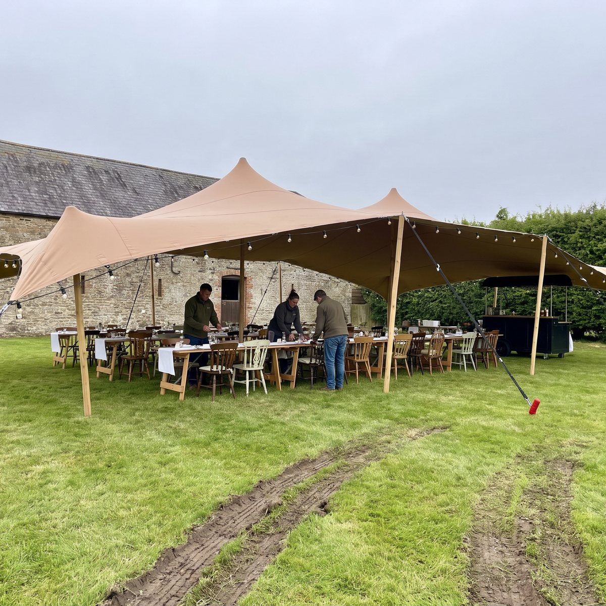 Sand-coloured stretch tent on wooden poles at a farm wedding